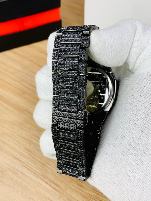 Luxury watch with a black diamond-studded strap held by a gloved hand on a wooden surface.
